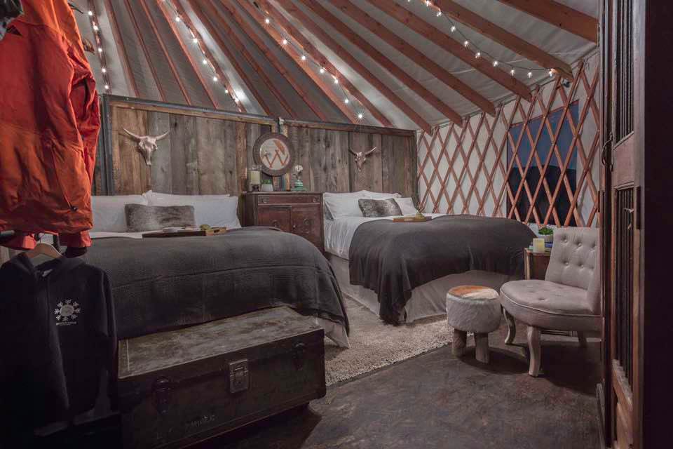 Rustic glamping-style yurt bedroom with exposed timber frame and warm textiles